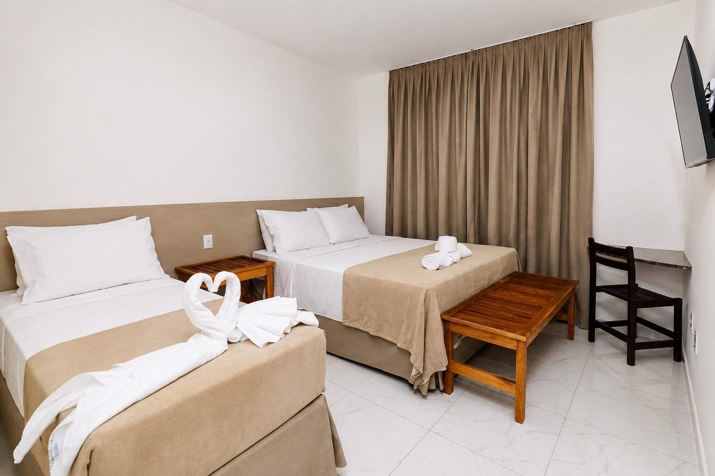 Cama de solteiro e cama de casal com banco de madeira, mesa e televisão no Quarto Triplo Standard