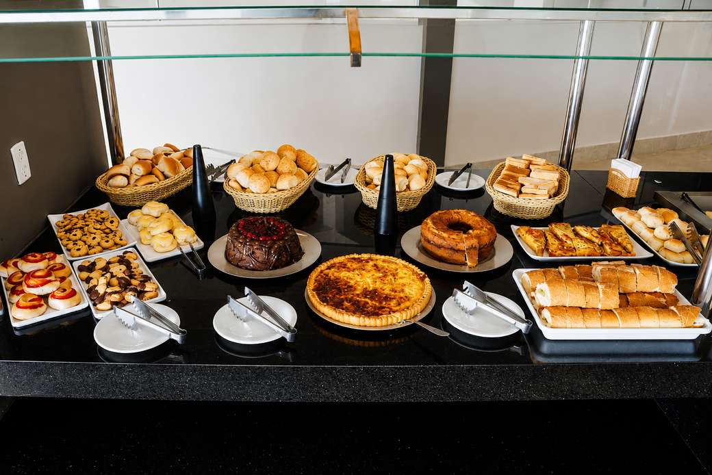 Balcão do buffet com pães, bolos, biscoitos e uma torta salgada
